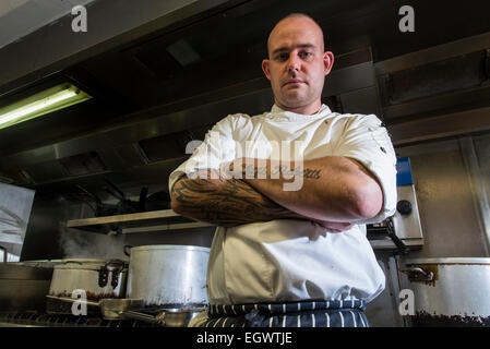 Un professionista significa ^ moody cercando chef sta nella sua cucina, guardando infastiditi con un sacco di apparecchiature di cottura in background Foto Stock