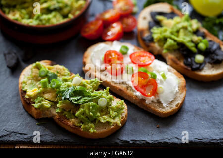 Crostini con diffusione di avocado, formaggio di capra e aglio nero Foto Stock