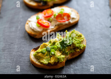 Crostini con diffusione di avocado, formaggio di capra e aglio nero Foto Stock