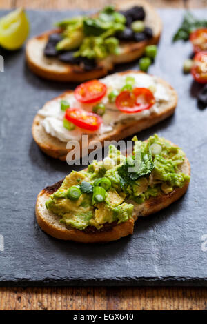 Crostini con diffusione di avocado, formaggio di capra e aglio nero Foto Stock