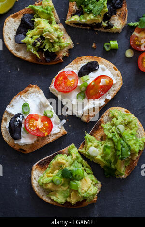 Crostini con diffusione di avocado, formaggio di capra e aglio nero Foto Stock