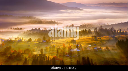 Sunrise, villaggio di montagna nella nebbia e tutto bello in una luce gialla Foto Stock
