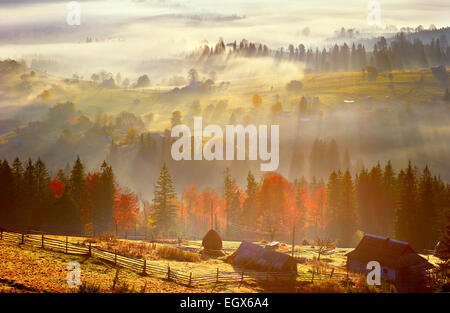 Sunrise, villaggio di montagna nella nebbia e tutto bello in una luce gialla Foto Stock