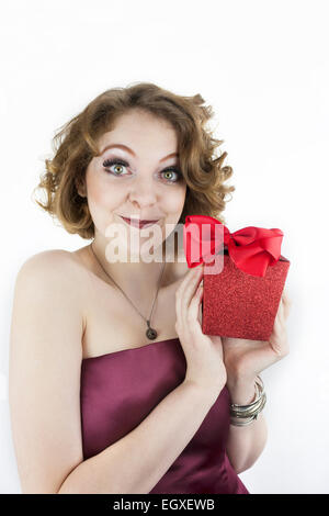 Piuttosto giovane donna che indossa senza spalline, borgogna dress holding scintillante, confezione regalo rossa con una prua Foto Stock