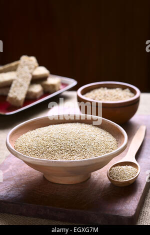 Bianco crudo quinoa (lat. Chenopodium quinoa) Semi di grano nella ciotola con la quinoa barrette di cereali nella parte posteriore sul pannello di legno Foto Stock