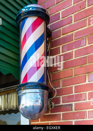 Barberia pole contro il mattone schierandosi con tenda verde Foto Stock