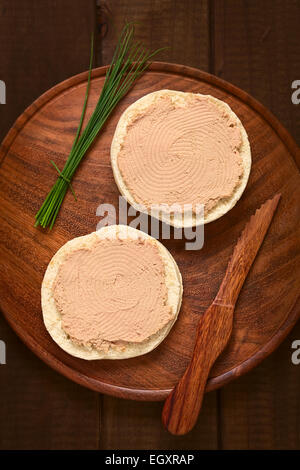 Tettuccio di colpo di liverwurst spalmato sul panino con erba cipollina e il coltello sul piatto di legno fotografati con luce naturale Foto Stock