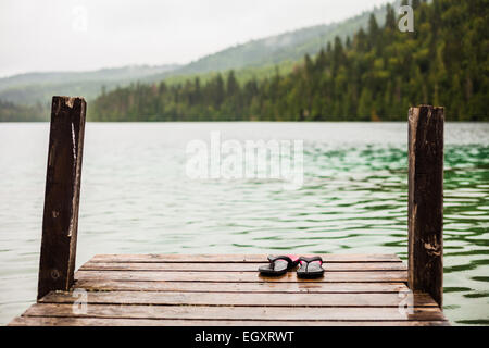 Il flip flop su un Dock nella parte anteriore di un'acqua turchese del lago nella natura selvaggia Foto Stock