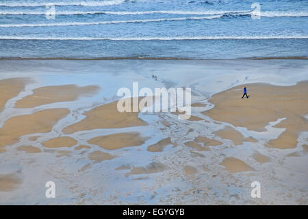 Un uomo cammina lungo una spiaggia di Newquay, Cornwall Foto Stock