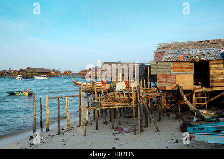 Sgangherato alloggiamento locale su palafitte oltre oceano con scuba diving resorts in background a Mabul Island, Borneo Foto Stock