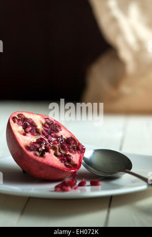 Still Life food immagine di un melograno su una piastra bianca con cucchiaino Foto Stock