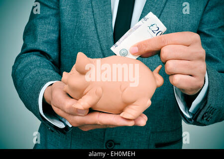 Primo piano di un giovane uomo che indossa una tuta introducendo una sterlina bill in un salvadanaio Foto Stock