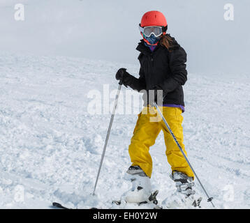 Ragazza giovane (9-11) sci di colore giallo luminoso pantaloni con casco arancione Foto Stock