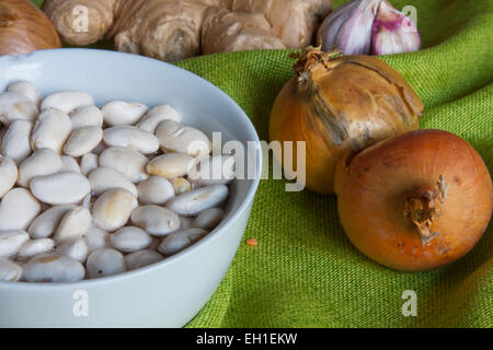 Fagioli bianchi sempre imbevuto di acqua. Accanto ad essa materie cipolle e altri ortaggi o legumi Foto Stock