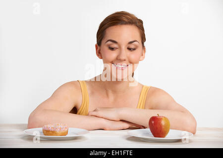 Giovane donna scegliendo tra ciambella e torta per snack Foto Stock