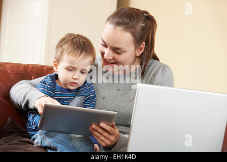 La madre lavora sul portatile mentre figlio Usa tavoletta digitale Foto Stock