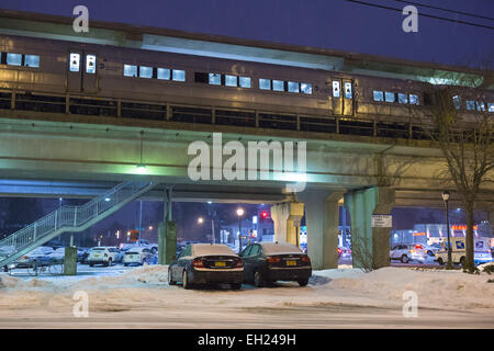 New York, New York, Stati Uniti d'America. 3 Mar, 2015. Durante il picco di sera i pendolari, un LIRR treno arriva sulla piattaforma sopraelevata come la neve cade a Merrick Long Island Rail Road LIRR stazione ferroviaria, di MTA, Mass Transit Authority. Un piccolo rosso bianco e blu posta USPS carrello è visto che viaggiano su Merrick Avenue sotto il cavalcavia del treno. La zona è al di sotto di un inverno Meteo Advisory e una tempesta di neve guarda per condizioni pericolose è in effetto dal Mercoledì notte al giovedì notte nel Long Island, New York City e di altre aree vicine del nord-est. © Ann Parry/ZUMA filo/Alamy Live News Foto Stock