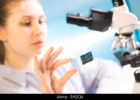 La donna in un microscopio da laboratorio con vetrino per microscopio in mano Foto Stock