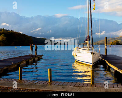 Barca a vela ormeggiata al pontile sul Lago di Windermere Parco Nazionale del Distretto dei Laghi Cumbria Inghilterra England Regno Unito con coppia in piedi sul molo Foto Stock