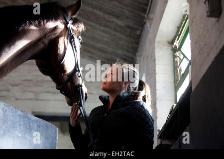 Una giovane donna in piedi in una stalla ammirando un cavallo Foto Stock