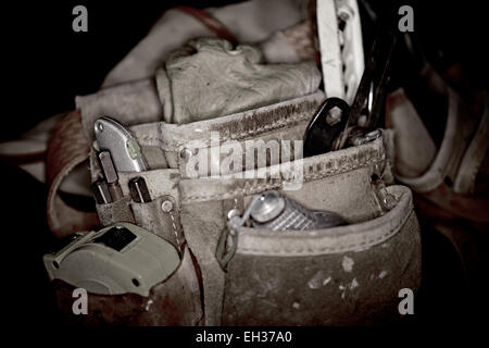 Primo piano di falegnami robusto cuoio lavoro borse e cinture con l uso di strumenti di costruzione isolata su sfondo nero Foto Stock