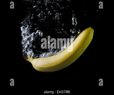 Banana gocciolata in acqua su sfondo nero. Le bolle di aria nell'acqua. Lavare la frutta. Foto Stock