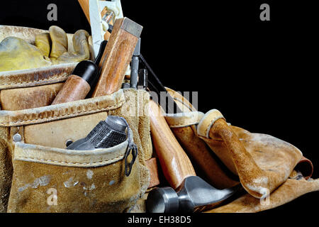 Robusto indossato i falegnami di lavori di cuoio borse e cinture con strumenti di costruzione e un martello isolato su nero Foto Stock