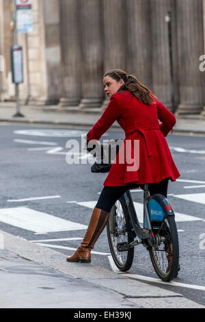 Giovane donna in rosso cappotto e stivali su un Boris Bike, Formalmente Conosciuti come Barclays Cycle Hire al di fuori della Banca di Inghilterra Foto Stock