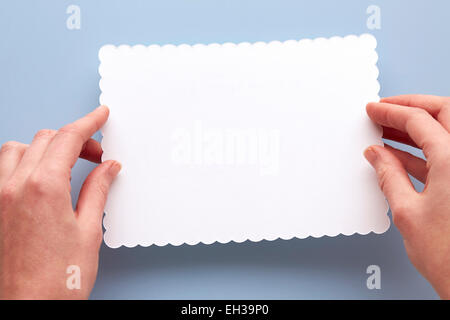 Donna di mani tenendo la scheda vuota con bordi frastagliati su sfondo blu Foto Stock