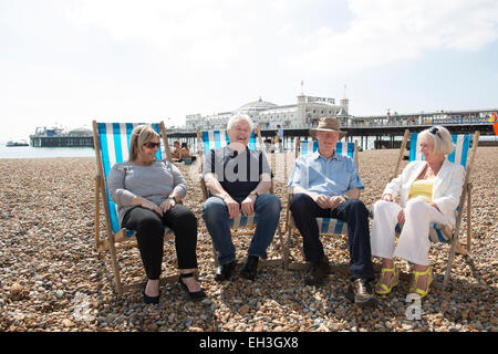 Un gruppo di persone di mezza età, sambuco, pensionamento più vecchi uomini e donne siedono sulla spiaggia di Brighton a parlare e ridere in sedie a sdraio Foto Stock