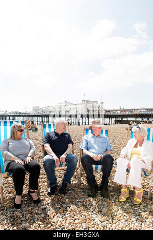 Un gruppo di persone di mezza età, sambuco, pensionamento più vecchi uomini e donne siedono sulla spiaggia di Brighton a parlare e ridere in sedie a sdraio Foto Stock