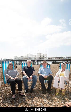 Un gruppo di persone di mezza età, sambuco, pensionamento più vecchi uomini e donne siedono sulla spiaggia di Brighton a parlare e ridere in sedie a sdraio Foto Stock