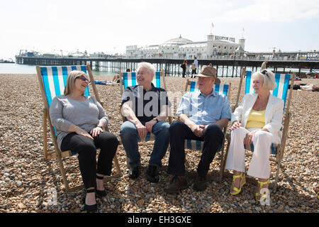 Un gruppo di persone di mezza età, sambuco, pensionamento più vecchi uomini e donne siedono sulla spiaggia di Brighton a parlare e ridere in sedie a sdraio Foto Stock