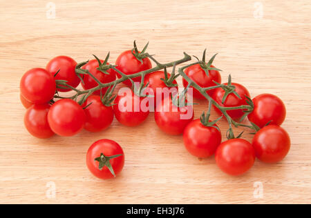 Piccolo piccolo pomodori ciliegia sulla vite su un legno chiaro dello sfondo. Foto Stock