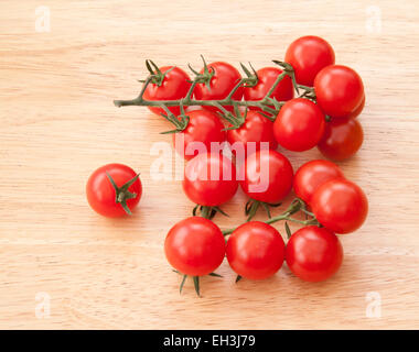 Piccolo piccolo pomodori ciliegia sulla vite su un legno chiaro dello sfondo. Foto Stock