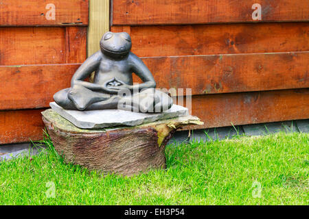 Il giardino di pietra a forma di rana meditando in un giardino seduto su un tronco di albero Foto Stock