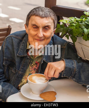 Disabilitato l'uomo con paralisi cerebrale seduti al cafe esterno con una tazza di caffè. Foto Stock