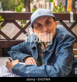 Disabilitato l'uomo con paralisi cerebrale seduta a outdoor cafe con un notebook e una matita. Foto Stock