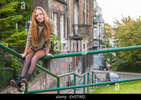 Giovani carino con i capelli lunghi ragazza seduta sul parapetto nella città vecchia. Foto Stock