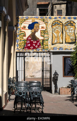 Svuotare outdoor cafe area con posti a sedere con un murale decorativo a Cienfuegos, Cuba. Foto Stock