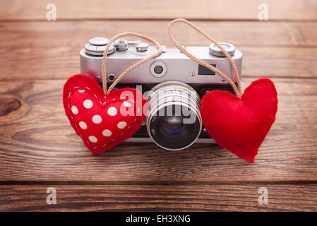 Fotocamera retrò con cuori rossi su sfondo di legno. Foto Stock