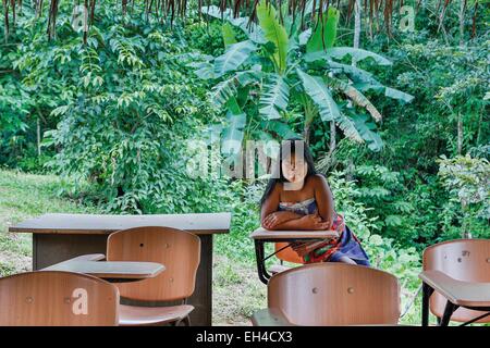 Panama, provincia di Darien, Parco Nazionale del Darién, classificato come patrimonio mondiale dall UNESCO, Embera comunità indigena, ritratto di una giovane Embera nativo in una vegetazione tropicale, seduti a un tavolo di scuola all'aperto Foto Stock