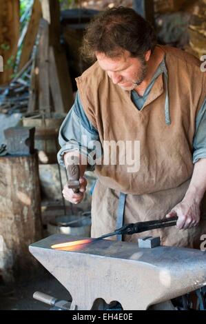 Francia, Yonne, La Puisaye, Treigny, Chateau de Guedelon, sito in costruzione di un castello medievale, fabbro sagomatura di un chiodo sulla sua incudine Foto Stock