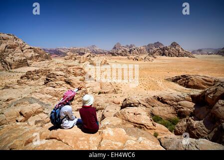 Giordania, Wadi Rum desert, area protetta elencati come patrimonio mondiale dall' UNESCO, turistici e locali guida beduino seduto su di una roccia, contemplando il paesaggio dal Monte Jebel Burdah Foto Stock