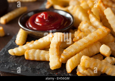 Malsana cotta Crinkle Patate fritte con Ketchup Foto Stock