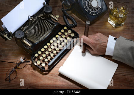 Primo piano di una scrittrice alla sua scrivania con una macchina da scrivere, telefono rotante, bicchiere di whiskey e un sigaro. Un'annata si sentono solo con il Foto Stock