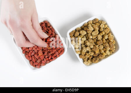 Donna takeand mangiare goji berry / wolfberry e mulberry da un vaso su sfondo bianco. Foto Stock