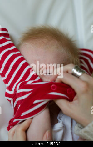Una 10-week-old baby boy infelice e irritato per essere vestito. Foto Stock