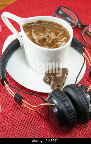 Tazza di caffè, cuffie e occhiali su una tovaglia rosso Foto Stock