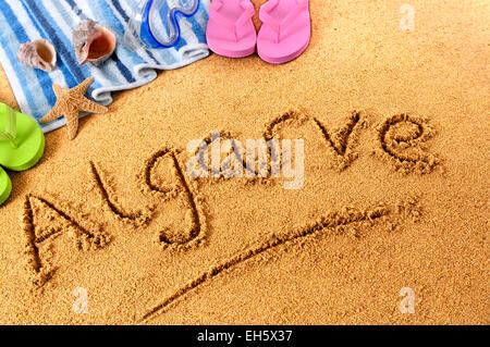 La parola Algarve scritto su una sabbiosa spiaggia del Portogallo, con telo mare, stelle marine e flip flop. Foto Stock